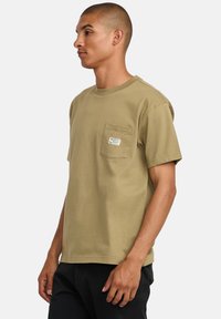 Olive green cotton T-shirt with short sleeves, crew neck, and a left chest pocket featuring a small label detail.