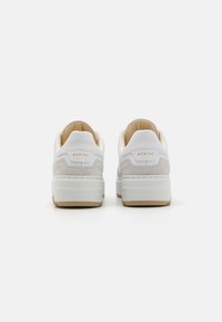 Adidași albi cu un capac de călcâi din suede gri texturat, accente bej și o talpă intermediară albă ridicată. Logo-ul brandului este embossat pe călcâi.