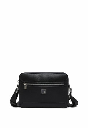 Bolso bandolera rectangular negro con bolsillo frontal con cremallera, herrajes plateados, correa ajustable y pequeña placa cuadrada con logo centrada debajo de la cremallera.