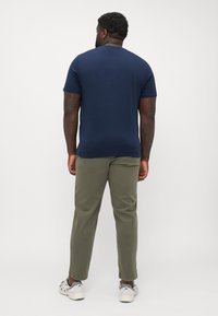 Mørkeblå kortærmet t-shirt parret med olivengrønne bukser. Sættet har en klassisk rund hals og en afslappet pasform. Fodtøjet består af grå og hvide sneakers.