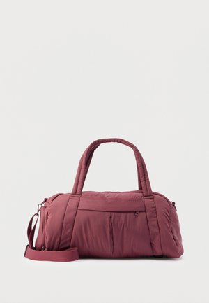 Bordó színű duffel táska puha, steppelt anyagból. Két füllel, levehető vállpánttal és az elején cipzáras zsebbel rendelkezik.