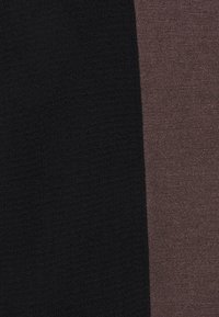 Nära bild av två stickade tygpaneler, en svart och en mörkbrun, förenade av en vertikal söm.