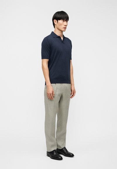 Μπλε ναυτικό πόλο μπλουζάκι με κοντό μανίκι και κλασικό γιακά, συνδυασμένο με ανοιχτό γκρι παντελόνι με στενή γραμμή και μαύρα επίσημα παπούτσια.