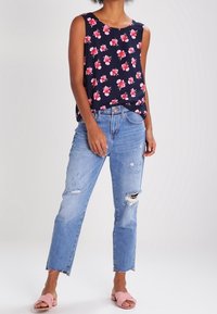Marineblaues Blumenshirt mit leuchtend pinken Blumen; kombiniert mit hellblauen, distressed Jeans mit ausgefransten Säumen; getragen mit pinken Slide-Sandalen.