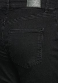 Jeans de mezclilla negra con una textura suave, que presentan un bolsillo trasero y detalles de costura sutiles. La etiqueta dice "Street One Studio."