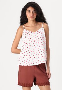 Top bianco senza maniche con pois rossi; design a scollo a V. Abbinato a pantaloni corti marroni con bordo in pizzo all'orlo. Tessuto morbido e leggero.