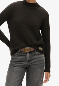 Pull en maille marron foncé avec un col et des poignets côtelés, associé à un jean gris taille haute et une ceinture marron avec une boucle en or.
