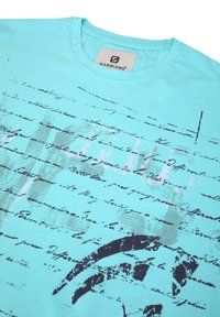 Camiseta Gabbiano de color azul claro con escritura a mano negra y un diseño gráfico desvanecido en la parte frontal.