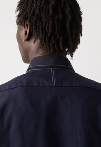 Navy shirt featuring a prominent collar, contrasting white stitching, and a smooth cotton texture. Viewed from the back.