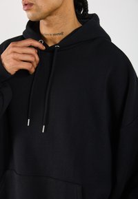 Sort hætte sweatshirt med løs pasform, der har en stor frontlomme, snore med metallisk spids og ribbede manchetter.