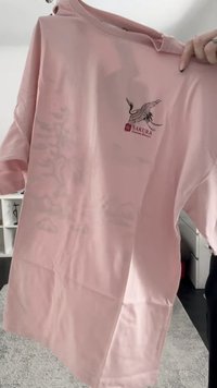 Light pink t-shirt featuring a logo with a crane design. Short sleeves, round neck, and soft fabric texture.