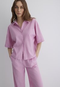 Pink striped short-sleeve shirt with a pocket, paired with matching loose-fit pants. Both items feature a textured, lightweight fabric.