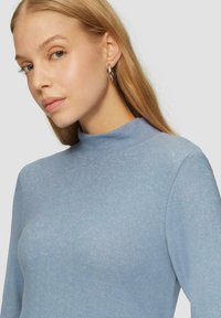 Helles Blau, langärmliger Rollkragenpullover aus weichem, strukturiertem Stoff. Verfügt über ein tailliertes Design mit hohem Kragen und subtiler glänzender Optik.