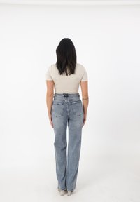 Top ajustado de color beige claro y jeans de mezclilla azul de tiro alto. Los jeans tienen pierna recta y dos bolsillos en la parte posterior. Tejido suave, diseño casual.