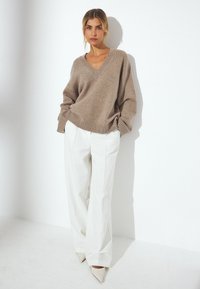 Beidzīgs v-line džemperis ar garām piedurknēm, pārspīlēts piegriezums, ribota apakša, apvienots ar baltām platām biksēm un punktētām beigtām papēžiem.