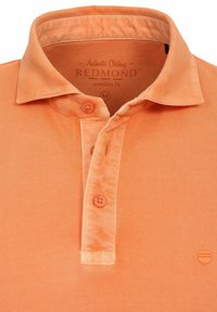 Orange polo shirt med tekstureret stof, tre-knaps lukning og et lille logoemblem. Med krave og en afslappet design.