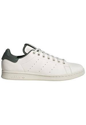 Zapatilla blanca de cuero con un talón de textil verde, puntera redonda, suela plana de goma y detalles perforados en el costado. Presenta cordones grises.