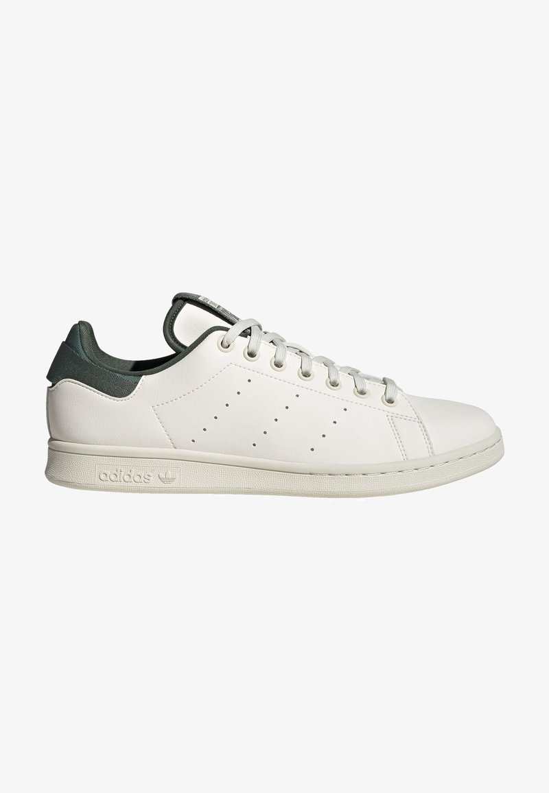 Zapatilla blanca de cuero con un talón de textil verde, puntera redonda, suela plana de goma y detalles perforados en el costado. Presenta cordones grises.