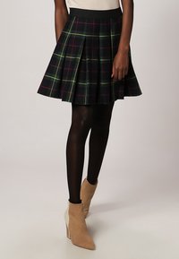 Falda de cuadro, hasta la rodilla, hecha de una mezcla de algodón. Presenta pliegues, una cinturilla negra y líneas verdes, rojas y amarillas sobre un fondo azul marino.