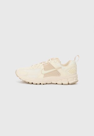 Baskets sportives beige et crème avec semelle texturée, empiècements en mesh, design à lacets, logo Nike sur le côté et languette au talon.