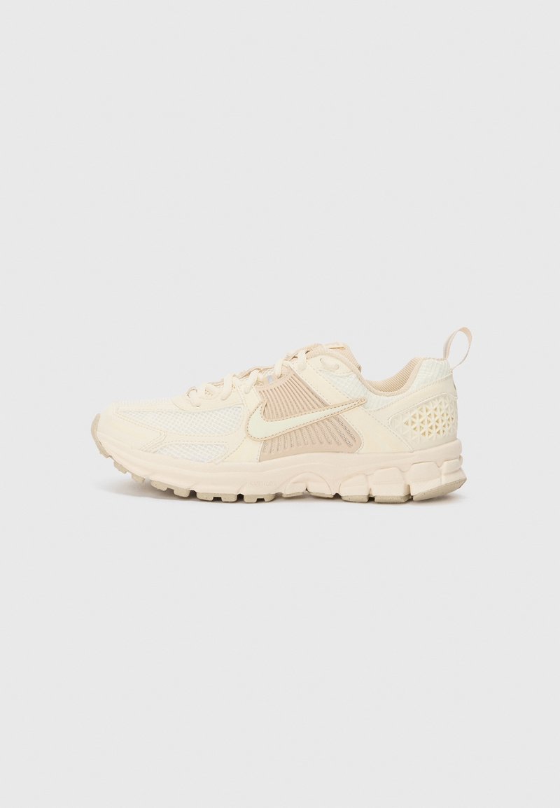 Baskets sportives beige et crème avec semelle texturée, empiècements en mesh, design à lacets, logo Nike sur le côté et languette au talon.