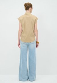 Camicetta beige a maniche corte con colletto, abbinata a jeans a gamba larga di colore blu chiaro. Il tessuto appare liscio con dettagli di cucitura visibili.