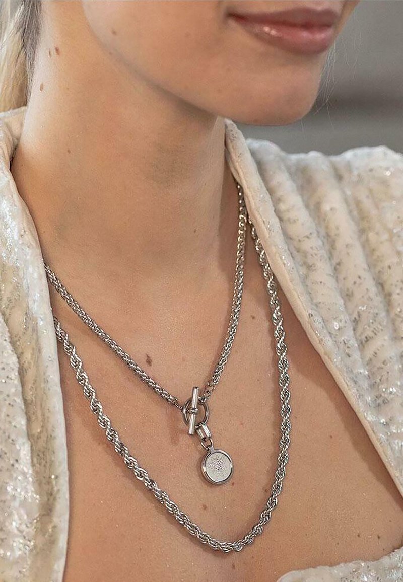 Colliers en argent à plusieurs couches présentant des chaînes torsadées et un pendentif rond avec des détails gravés, mettant en avant un design élégant et moderne.