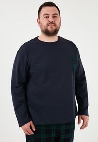 Tumesinine pikakä sleeve särk rohelise ruudulise taskuga. Pehme materjal, ümar kaelus ja lõdvemaist. Kantud ruuduliste ööriietega.
