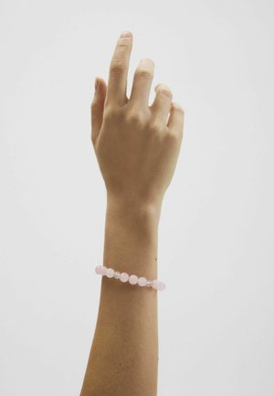 Mano sollevata con le dita leggermente piegate, che indossa un braccialetto rosa con perline al polso, su uno sfondo bianco uniforme.