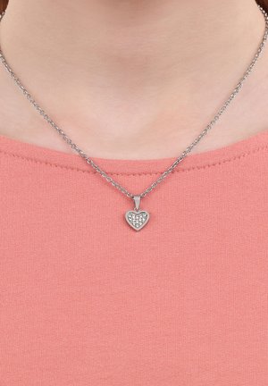 Collar de cadena de plata con un colgante en forma de corazón adornado con pequeños patrones de corazones y rhinestones, que se lleva sobre una blusa color coral.