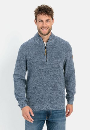 Blue knitted sweater with a half zip, featuring a textured pattern and ribbed cuffs. Worn with blue jeans, simple design without embellishments.