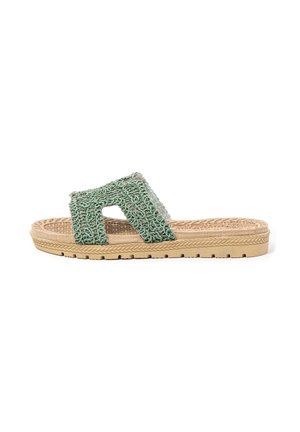 Sandalia de slide beige con suela texturizada y tira tejida verde con aberturas laterales, aislada sobre fondo blanco.