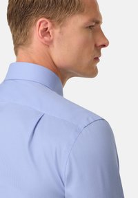 Camicia a scacchi blu chiaro con colletto classico, vestibilità su misura e tessuto liscio, mostrata da un'angolazione laterale.
