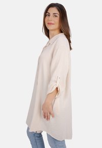 Hellbeige Hemd mit Knöpfen aus strukturiertem Stoff, mit umgestülpten Ärmeln und gebundenen Akzenten, in lockerer Passform, kombiniert mit blauen Jeans.