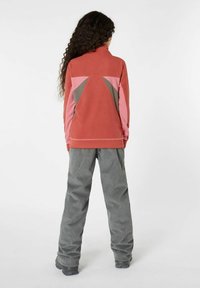 Veste en polaire corail et rose avec des accents gris, présentant un col montant et un design géométrique au dos. Associée à un pantalon en velours cordé gris.