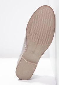 Chaussure à semelle plate avec une tige beige clair, dotée de détails cousus. La semelle est texturée avec des rainures horizontales pour l'adhérence. Taille 37.