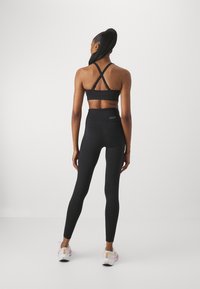Schwarzer Sport-BH mit gekreuzten Trägern, hoch taillierte schwarze Leggings und weiße Sportschuhe mit rosa Akzenten. Glattes, dehnbares Material.