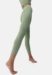 Lys grønne leggings laget av elastisk stoff, med buede sømmer for en tett passform og en bred midje for komfort.