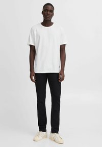 Witte katoenen t-shirt met korte mouwen en een ronde halslijn, gecombineerd met zwarte jeans en beige sneakers. Eenvoudig ontwerp, geen zichtbare patronen.