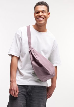 Sac bandoulière en tissu lavande doux et atténué avec une texture lisse, doté d'une large sangle et d'un design minimaliste. Porté en travers du corps.