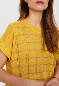 Gul stickad topp med lös passform, med rosa horisontella ränder och öppet mönster. Korta ärmar och ribbat halsband.