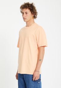  ferskenfarvet bomulds t-shirt med rund hals, korte ærmer og en afslappet pasform. Har et lille logo på brystet og en glat overflade.