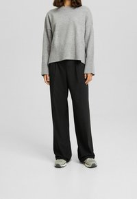 Jasnoszary sweter robiony na drutach z szerokim ściągaczem, zestawiony z luźnymi czarnymi spodniami i szarymi trampkami. Prosty, casualowy strój.