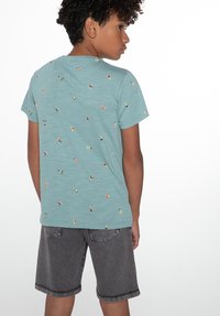 Šviesiai mėlynas trumpas rankovėmis marškinėliai su išbarstytais spalvingais raštais, derinami su pilkais šortais, turinčiais klasikinį kirpimą ir kišenes.