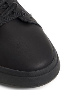 Mustat nahkakengät, joissa on teksturoitu pinta, pyöreä kärki, vahvistettu kumipohja ja mustat nauhat, jotka on pujotettu pyöreisiin reikiin.