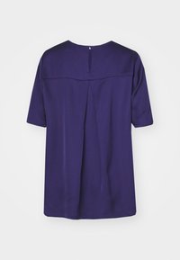 Lila kurzärmliges Oberteil mit einem Schlüsselrücken-Detail, Falten in der Mitte und glattem, gewebtem Material. Einfaches Rundhalsdesign.
