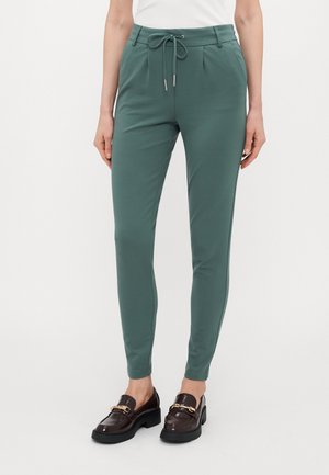 Grønne joggebukser laget av myk stoff, med snøring i livet, avsmalnede ben og side søm detaljer. Brukt med mørke loafers.