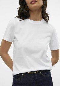 T-shirt en coton blanc à manches courtes et col rond, porté avec un jean en denim foncé et une ceinture dotée d'une boucle dorée.