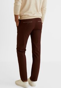 Brązowe spodnie z miękkiego materiału o zwężanym kroju. Posiadają dwie tylne kieszenie z zapięciami na guziki i srebrne akcenty. W zestawie z białymi butami.