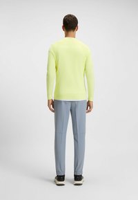 Jasnożółta bluzka z długim rękawem w połączeniu z jasnoniebieskimi spodniami typu tapered. Strój charakteryzuje się minimalistycznym designem z elastycznymi mankietami i bez widocznych wzorów.